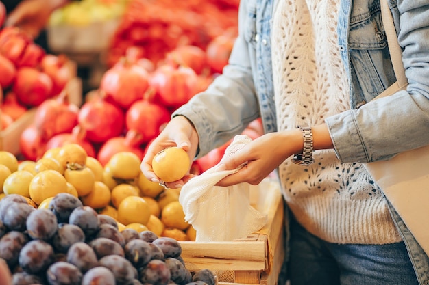 Les mains des femmes mettent les fruits et légumes dans un sac de produits en coton au marché alimentaire. Sac écologique réutilisable pour faire du shopping. Mode de vie durable. Concept écologique.