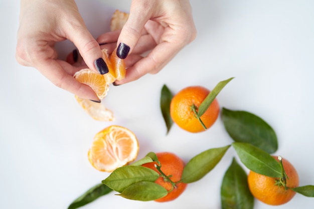 Mains de femmes nettoyant mandarine. Les mandarines fraîches orange avec des feuilles vertes se trouvent.