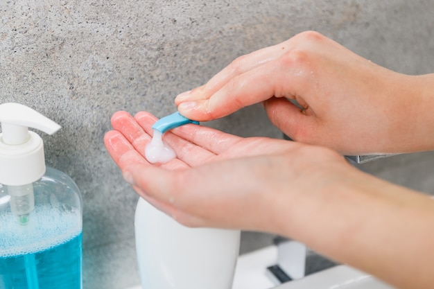 Les mains des femmes prennent du gel de savon pour se laver les mains au robinet et à l'évier de la salle de bain à domicile pour protéger la peau contre les virus et les microbes pendant l'épidémie de coronavirus