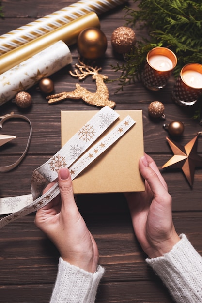 Les mains des femmes ramassent un ruban festif pour emballer un cadeau de noël bricolage passe-temps