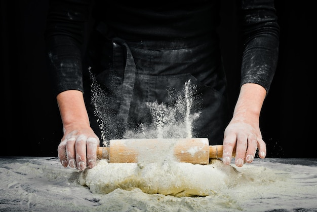 Les mains des femmes avec un rouleau à pâtisserie préparent la pâte pour le pain ou la pizza. Fond de cuisine noir.