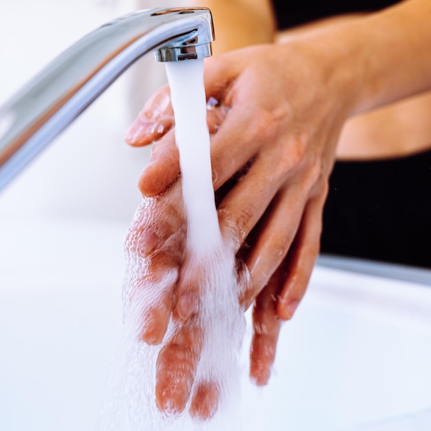 Les mains des femmes sous l'eau du robinet en gros plan, mise au point sélective douce. Se laver les mains sous l'eau courante, hygiène