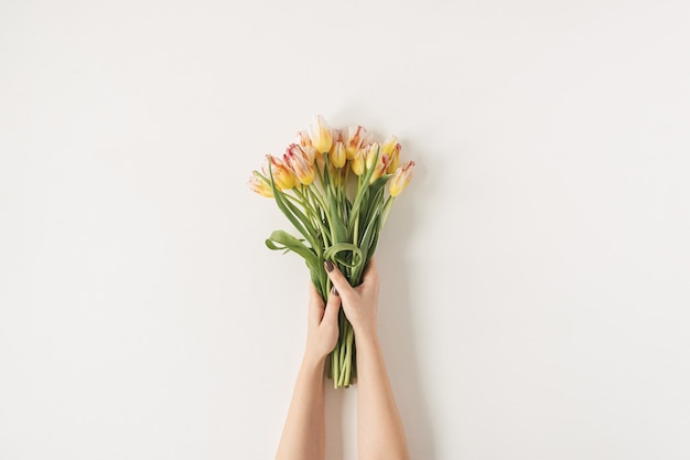 Les mains des femmes tenant le bouquet de fleurs de tulipes contre le mur blanc