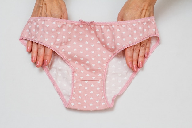 Photo mains de femmes tenant une culotte en coton rouge sur fond blanc. ensemble de sous-vêtements femme. vue de dessus.