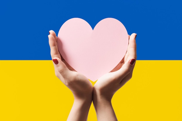 Mains de femmes tenant du papier en forme de coeur sur fond de couleur du drapeau de l'Ukraine Restez avec le symbole de l'ukraine