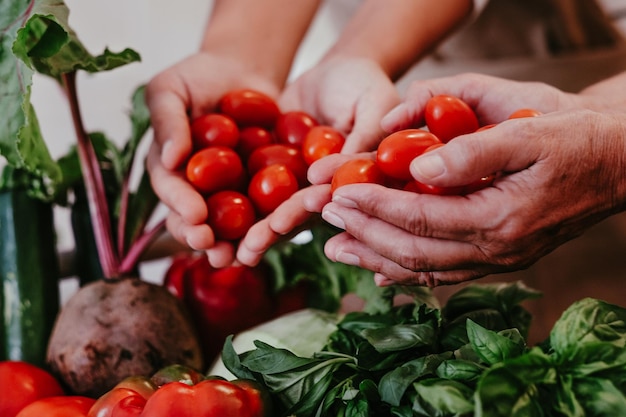 Mains de femmes tenant de petites tomates rouges. Panier plein de légumes frais et crus. Concept sain, végétalien, végétarien, de désintoxication, de régime