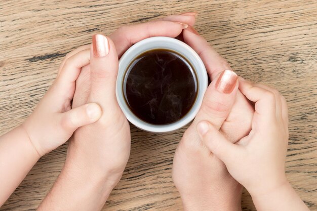 Mains de femmes tenant une tasse de café chaud dans les mains des enfants sur une vieille table en bois vintage