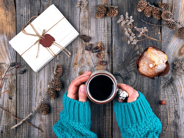 Mains de femmes tenant une tasse en céramique avec un café noir et une table en bois grise