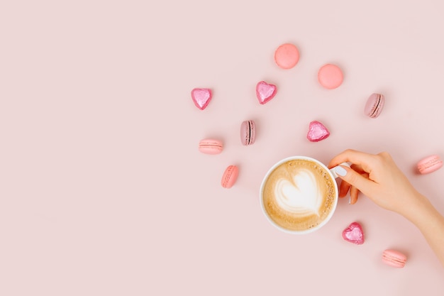 Les mains des femmes tiennent l'art du cappuccino sur fond rose pâle