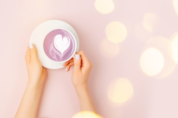 Les mains des femmes tiennent l'art du cappuccino sur fond rose pâle