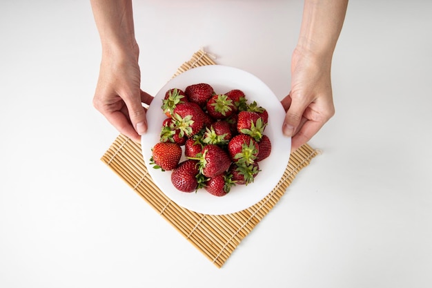 Les mains des femmes tiennent une assiette avec des fraises sur un fond de tableau blanc Vue de dessus mise à plat