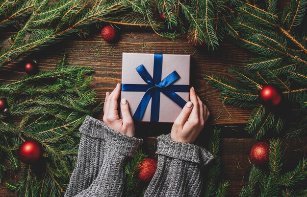 Les mains des femmes tiennent la boîte-cadeau à côté de la décoration de Noël sur une table