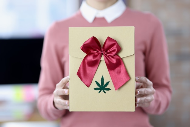 Les mains des femmes tiennent la boîte avec le logo de l'arc et de la marijuana