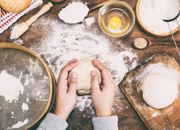 Des mains de femmes tiennent une boule de pâte à levure sur une table