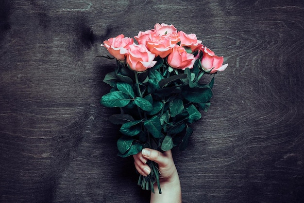 Les mains des femmes tiennent un bouquet romantique de roses roses tendres sur fond de bois