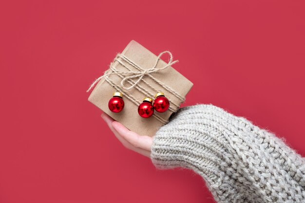 Les mains des femmes tiennent des coffrets cadeaux en papier Kraft avec un décor de Noël sur fond rouge, gros plan. Fond de nouvel an. Emballage cadeau en matériaux naturels dans un style rétro, vintage et tendance.