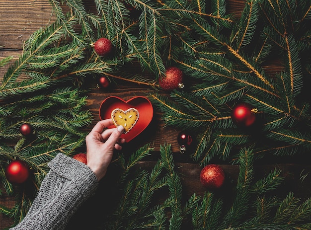 Les mains des femmes tiennent le cookie à côté des branches d'arbres de Noël et des boules autour