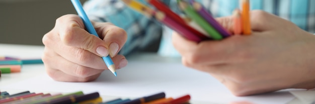 Les mains des femmes tiennent des crayons multicolores et une feuille de papier se trouve sur la table