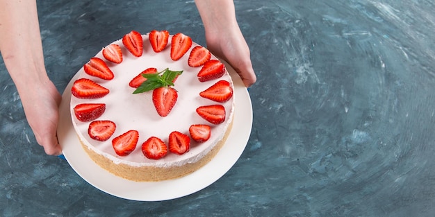 Les mains des femmes tiennent un délicieux gâteau au fromage avec des fraises fraîches et une recette maison à la menthe sans cuisson sur une table en pierre bleu foncé Copier l'espace