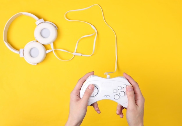 Les mains des femmes tiennent des gempads rétro sur fond jaune avec un casque Concept de jeu