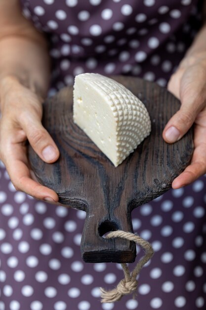 Les mains des femmes tiennent un gros morceau de fromage cottage fait maison sur une planche de cuisine vintage