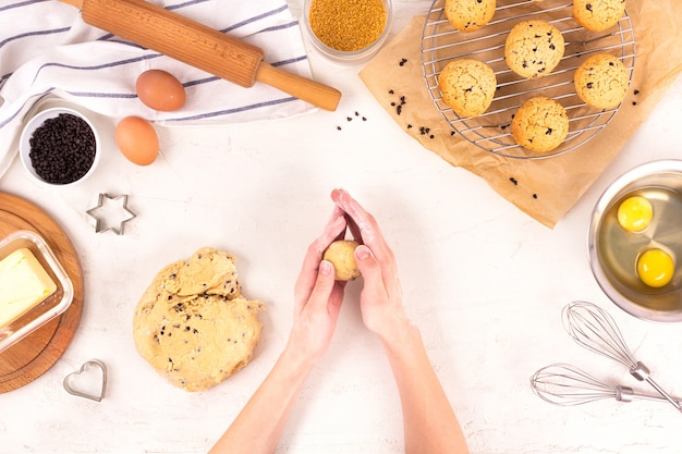 Les mains des femmes tiennent la pâte pour faire des biscuits. Equipement et ingrédients culinaires. Œufs, farine, sucre, chocolat, beurre, plats de cuisson. Lay plat.