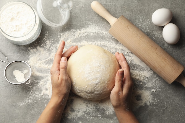 Les mains des femmes tiennent la pâte sur une surface grise avec des ingrédients pour la cuisson