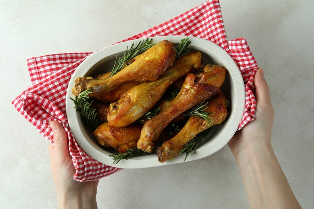 Les mains des femmes tiennent la plaque de cuisson avec des pilons de poulet rôti