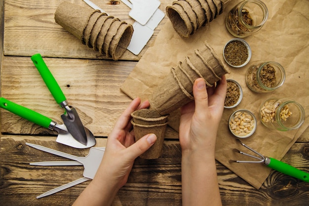 Les mains des femmes tiennent des pots de tourbe Vue de dessus des graines et des outils de jardin sur un fond en bois