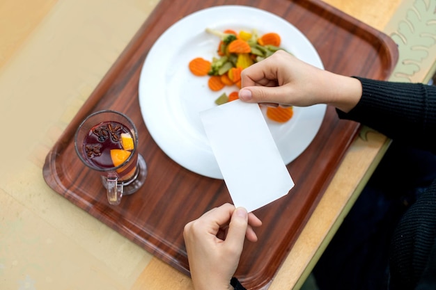 Les mains des femmes tiennent le reçu sur un plateau avec une assiette et un thé aux fruits