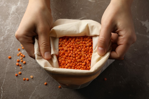 Les mains des femmes tiennent le sac de légumineuses rouges sur table grise