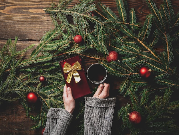 Les mains des femmes tiennent tasse de thé et boîte-cadeau avec arbre de Noël sur une table