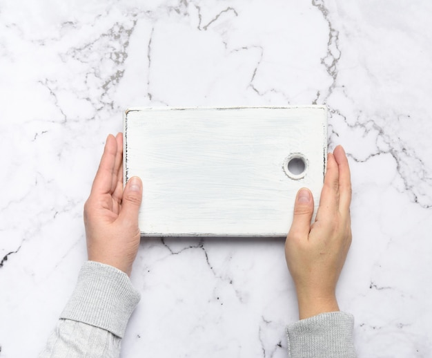 Les mains des femmes tiennent une vieille planche à découper en bois rectangulaire blanc vide, vue du dessus