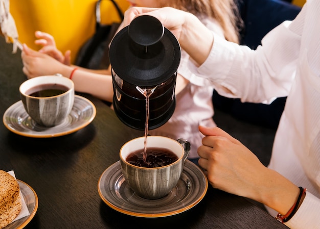 Les mains des femmes versent le thé d'une théière dans de belles tasses. Tea party dans un café.