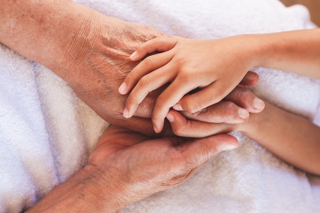 Mains de fille asiatique enfant tenant mains de grands-parents âgés peau ridée avec soin et amour