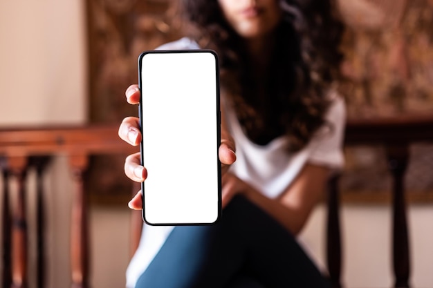 Mains d'une fille assise sur une chaise avec un écran blanc de smartphone