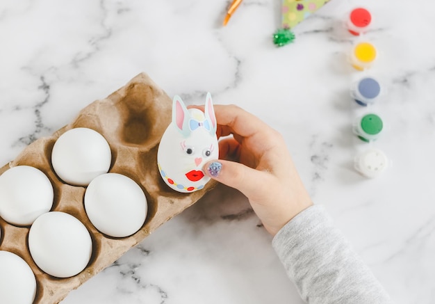 Mains d'une fille caucasienne dans un col roulé gris portant un œuf de lapin de Pâques avec des autocollants dans une boîte en carton