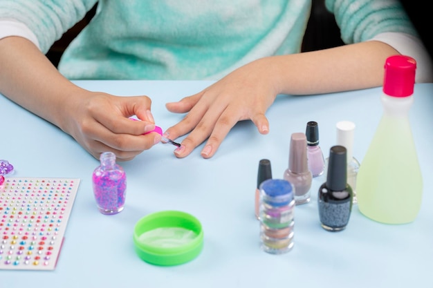 Mains d'une fille peignant ses ongles avec du vernis sur une table bleue