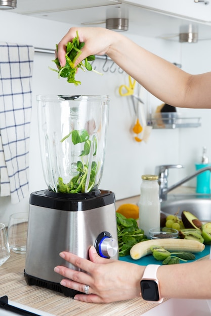 Les mains de la fille préparent un smoothie vert, met des feuilles d'épinards fraîches dans un mélangeur. Concept de saine alimentation. Végétarisme, nourriture végétalienne, nourriture de fitness, désintoxication, préservation de la jeunesse.