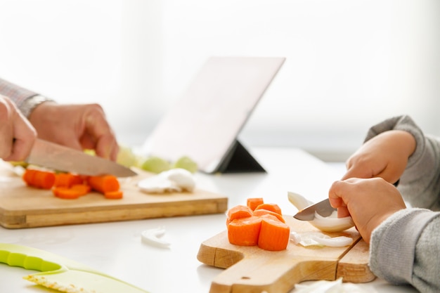 Les mains d'une fille et son père préparent des aliments dans la cuisine avec une tablette en arrière-plan