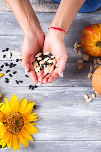 Mains d&#39;une fille tenant des graines de tournesol et une citrouille sur un fond en bois gris