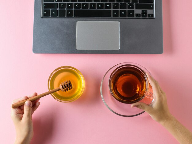 Mains de filles avec du miel et une tasse de thé devant l'ordinateur. La vue d'en haut.