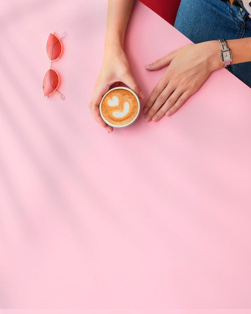 Les mains des filles tiennent une tasse de café sur fond rose