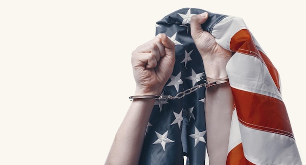 Les mains sur un fond blanc serrées dans un poing avec des menottes attachées dessus, les mains s'accrochent au drapeau américain