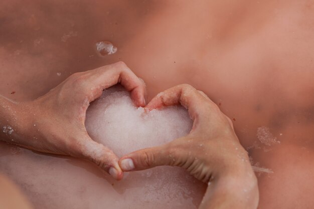 les mains en forme de coeur des femmes tiennent du sel rose sur la surface de l'eau d'un lac rose unique