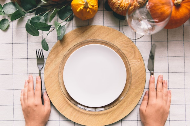 Mains avec fourchette et couteau, assiette blanche sur la table.