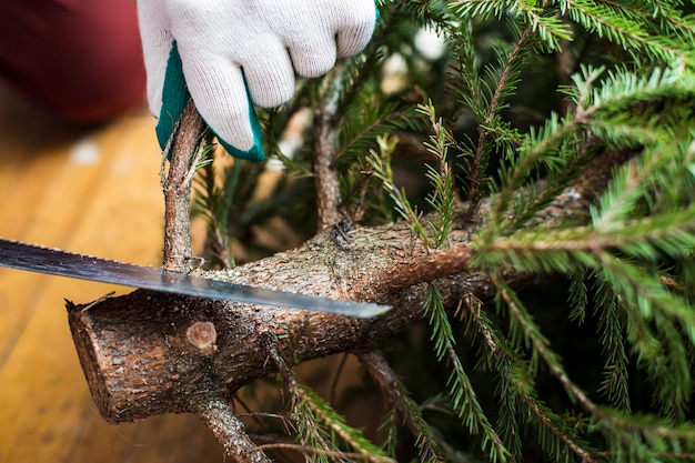 Mains gantées à l'aide d'une scie pour couper des branches au bas de l'arbre de Noël Préparation pour le Nouvel An