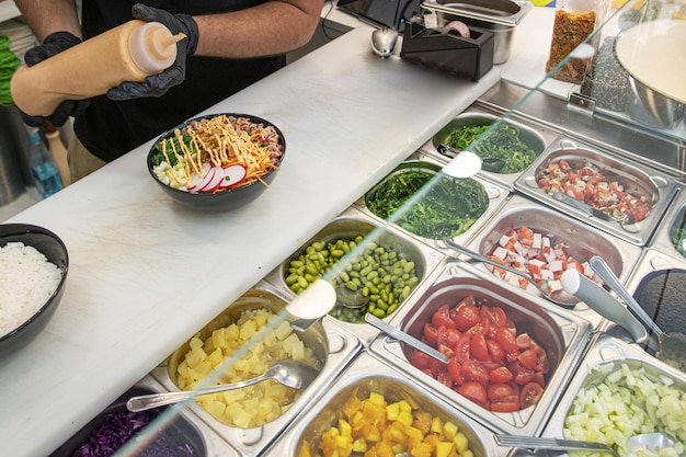 Photo les mains gantées du chef mettent la touche finale à un poke bowl hawaïen plateaux en métal avec des ingrédients frais