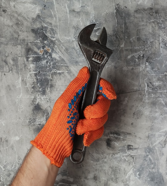 Les mains avec des gants de travail tiennent une clé sur fond de béton gris. Ouvrier industriel