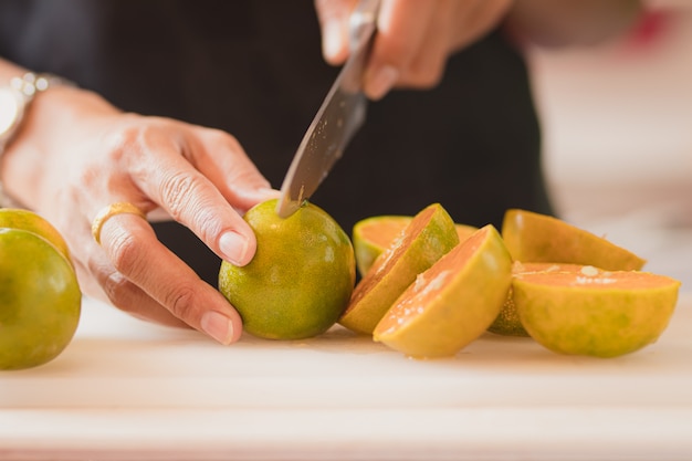 les mains des gens coupent des oranges.